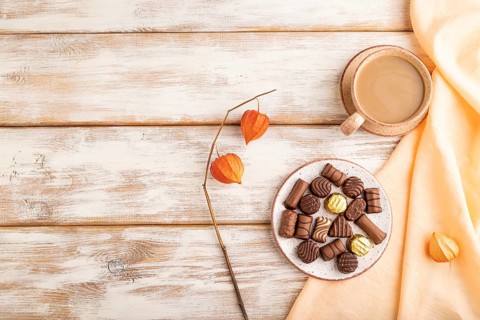 Chocolate candies with cup of coffee and physalis flowers on a white wooden background and orange