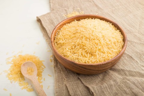 Wooden bowl with raw golden rice and wooden spoon on a white wooden background and linen textile.