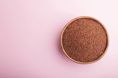 Wooden bowl with raw red quinoa seeds on a pastel pink background. Top view, flat lay, copy space