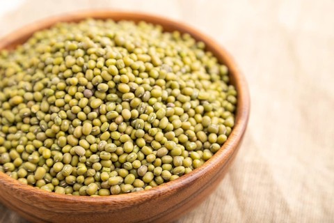 Wooden bowl with raw green mung bean on a white background and linen textile. Side view, close up,
