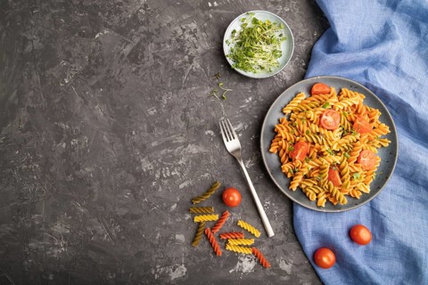 Tortiglioni semolina pasta with tomato and microgreen sprouts on a black concrete background and