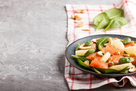 Fresh salmon with pineapple, spinach and cashew on a gray concrete background. Side view, copy