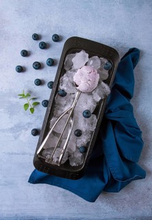 Blueberry ice cream, container with a spoon, on a gray table, fresh blueberries