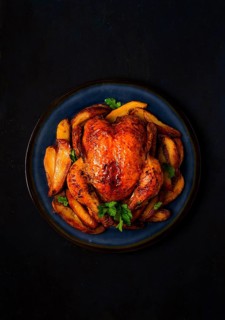 Fried whole chicken, with potatoes, on a black background, no people