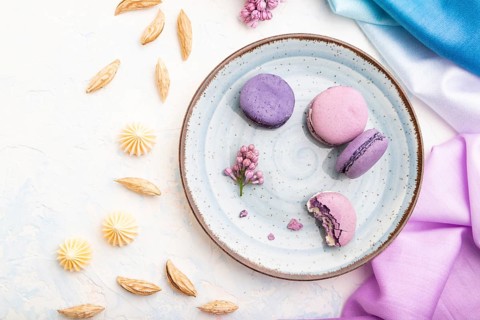 Purple macarons or macaroons cakes with cup of coffee on a white concrete background and