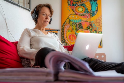 Woman, mid-50s, works from home, with laptop and communicates with colleagues via headset, home