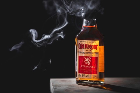 A single whisky bottle with smoke against a dark background