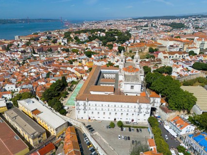 Aerial view of a coastal town with red roofs, white buildings, a bridge and green trees, aerial