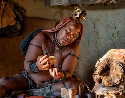 Traditional Himba woman prepares herbs for body care with smoke, interior of the first woman's mud