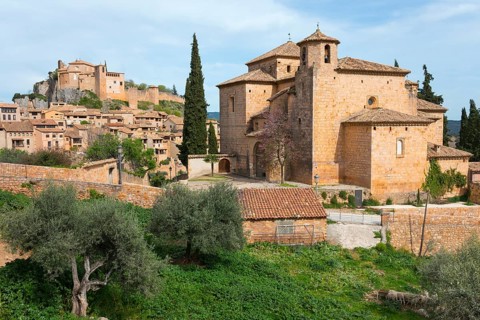 A historic town with medieval buildings and a stone church surrounded by cypresses and trees under