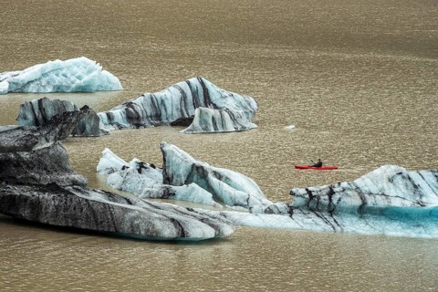 Single kayaker in red kayak, glacial lake at the glacier solheimajökull, icebergs on the lake,