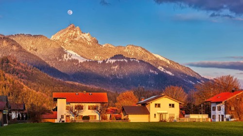 Sunset over an alpine scene with houses in the foreground, snow-covered mountain in the background