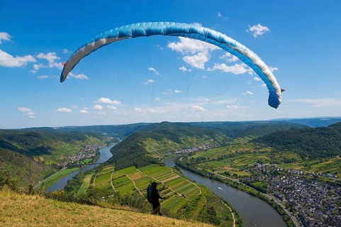 A paraglider takes off over a picturesque river landscape under a blue sky, paragliding, Bremm,