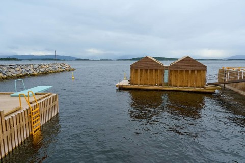 Outdoor sea pool by the fjord with small wooden sauna huts, overcast sky and calm water, Molde,