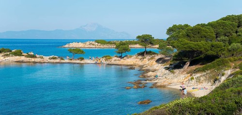Picturesque coastal landscape with rocky beach and trees in front of clear blue water, Karidi