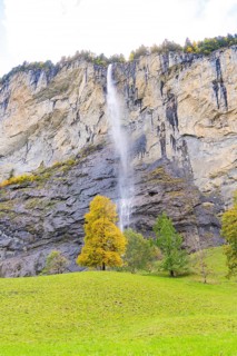 A waterfall flows down from high rocks, surrounded by trees in autumnal colours, Lauterbrunnen,