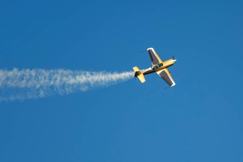Golden stunt aerobatic plane performing stunts in blue sky with smoke trail. Concept of speed,