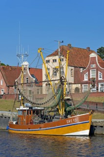 Crab cutter in the harbour in front of historic buildings, blue sky, Greetsiel, North Sea, Lower