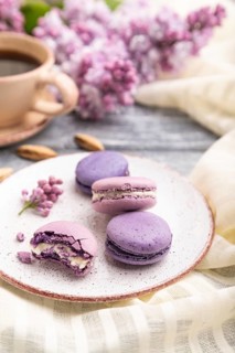 Purple macarons or macaroons cakes with cup of coffee on a gray wooden background and white linen