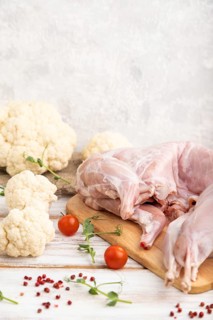 Whole raw rabbit with cauliflower, tomatoes and spices on a white wooden background and linen