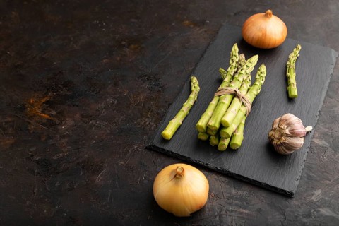 Bunch of fresh green asparagus, garlic, onion on slate board on black concrete background. Side