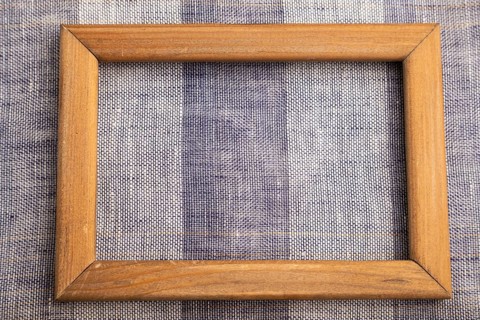 Wooden frame on smooth brown and violet linen tissue. Top view, flat lay, natural textile