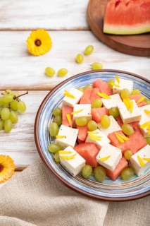 Vegetarian salad with watermelon, feta cheese, and grapes on blue ceramic plate on white wooden