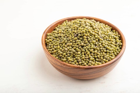 Wooden bowl with raw green mung bean on a white wooden background. Side view, close up