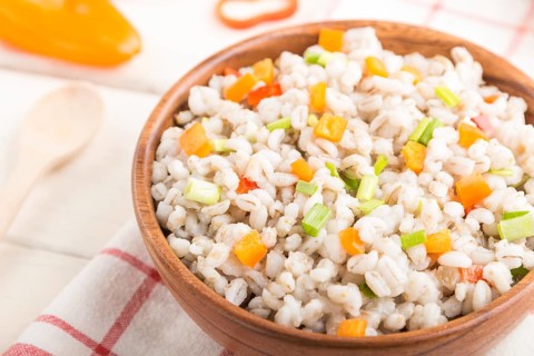 Pearl barley porridge with vegetables in wooden bowl on a white wooden background and linen textile