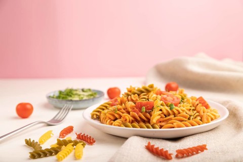 Tortiglioni semolina pasta with tomato and microgreen sprouts on a white and pink background and