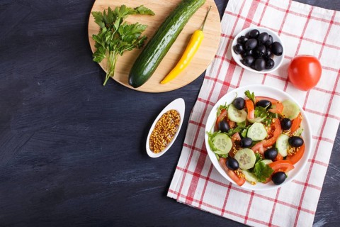 Vegetarian salad of tomatoes, cucumbers, parsley, olives and mustard on linen tablecloth and black