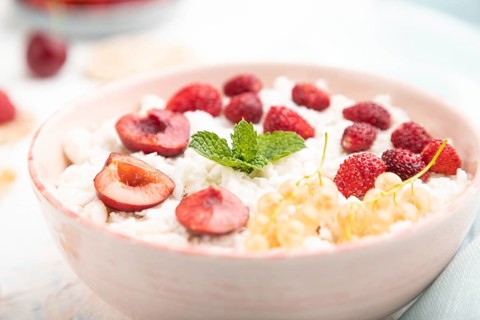 Rice flakes porridge with milk and strawberry in ceramic bowl on white concrete background and blue