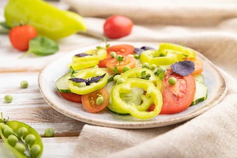 Vegetarian salad from green pea, tomatoes, pepper and basil on white wooden background and linen