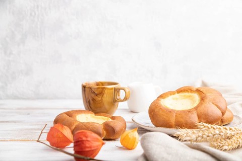 Sour cream bun with cup of coffee on a white wooden and concrete background and linen textile. Side