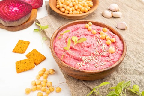 Hummus with beet and microgreen basil sprouts in wooden bowl on a white wooden background and linen