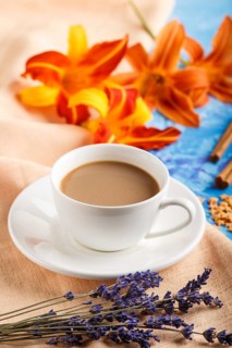 Orange day-lily and lavender flowers and a cup of coffee on a blue concrete background, with orange