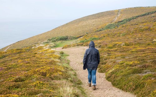 Woman wearing kagoule walking along the South West coast path at St Agnes head, Cornwall, England,