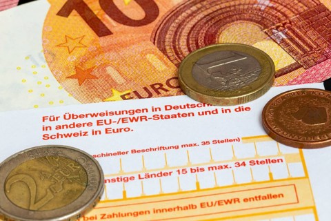 Symbolic image of payment transactions: close-up of a transfer form with euro coins and euro notes