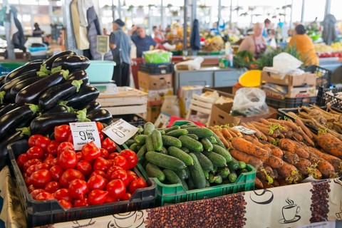 Colourful display of vegetables at a market stall with price tags and background activity, market
