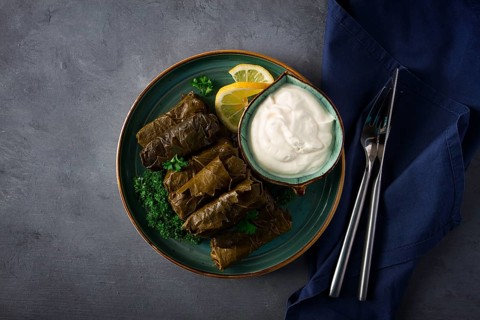 Dolma, cabbage rolls, grape leaves with filling, white sauce, lemon and herbs, rustic, selective
