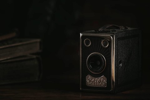 Old box camera against a dark background next to old books