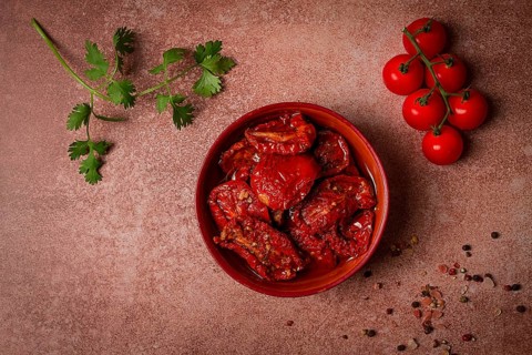 Dried tomatoes, in a bowl, top view, on a brown background
