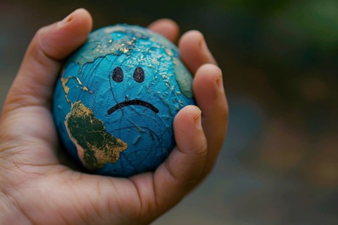 Small planet earth globe with sad face held by hand. Generative Ai, AI generated