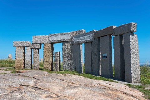 Circular stone structure, standing under a clear blue sky with nature in the background, Monumento