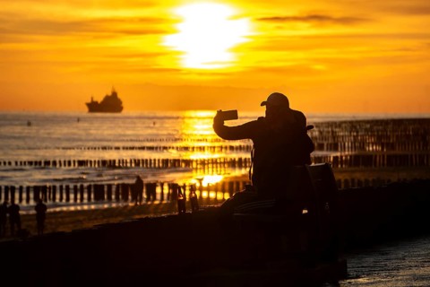 Sunset on the beach of Zoutelande, beach with wooden pile breakwaters, tourists, cargo ship sailing