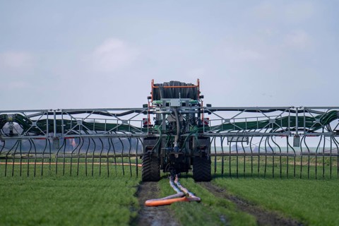Tractor with boom for spreading liquid manure, on a field, fertilisation