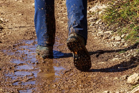 A person in hiking boots on a muddy path outdoors