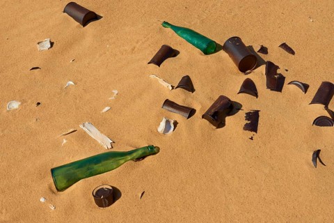 Broken glass bottles and rubbish on sand showing pollution in a desert, Matruh, Great Sand Sea,