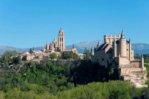 Medieval city with castle and cathedral, surrounded by trees and mountains in sunny weather,