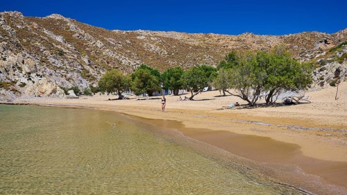 Quiet beach with clear water and golden sand, surrounded by trees and rocks under a deep blue sky,